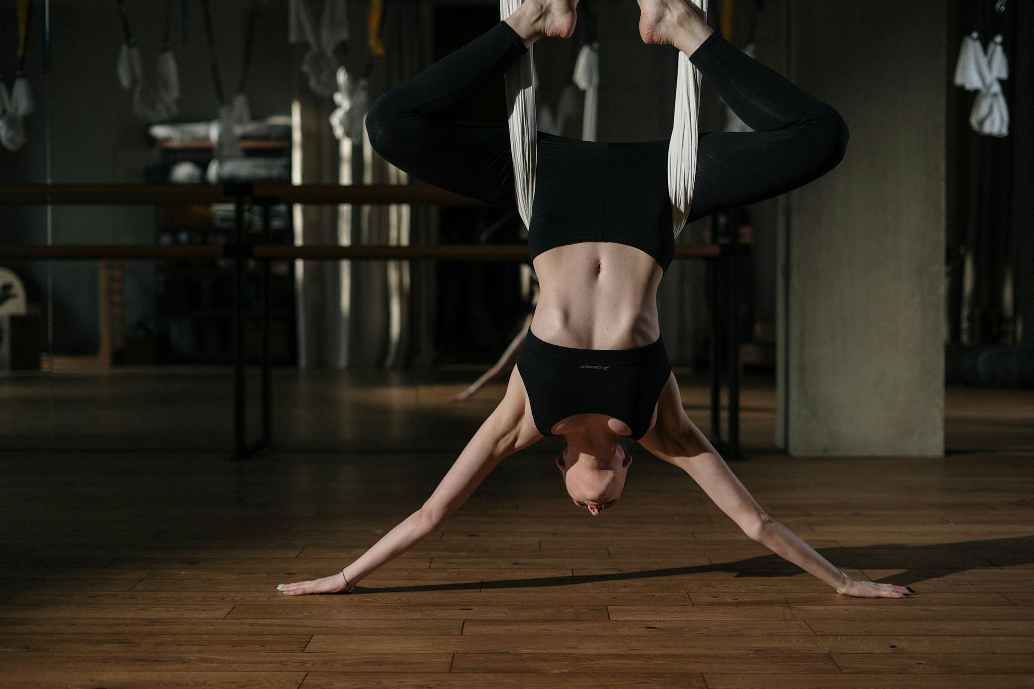 A woman practices aerial yoga pose upside down in a sunlit studio, showcasing strength and flexibility.